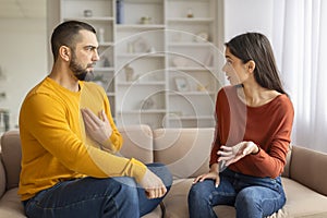 Young Couple Having Emotional Conversation While Sitting On Couch At Home