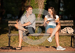 Young couple having fun on a bench in park while socializing over web