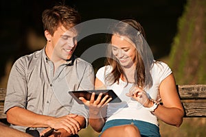 Young couple having fun on a bench in park while socializing over web