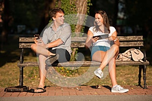 Young couple having fun on a bench in park while socializing over web