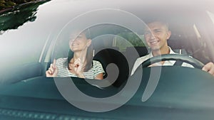 Young couple having fun in a car. Fun, sing and dance. The windshield reflects trees and clouds when driving a car