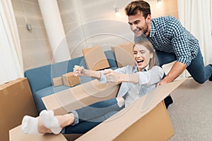 Young couple having fun while moving to new apartment. Moving newlyweds. Girl is sitting in a box.