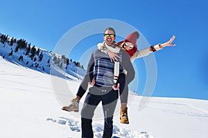 Young couple having fun on snow. Happy man at the mountain giving piggyback ride to his smiling girlfriend.