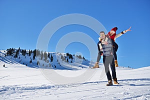 Young couple having fun on snow. Happy man at the mountain giving piggyback ride to his smiling girlfriend.