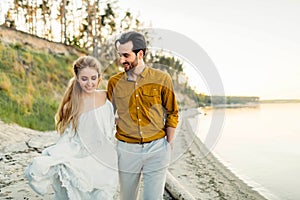 A young couple is having fun and walking on the sea coastline. Newlyweds looking at each other with tenderness. Romantic