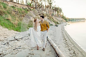 A young couple is having fun and walking on the sea coastline. Newlyweds looking at each other with tenderness. Romantic