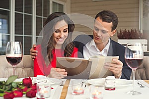 Young couple having romantic dinner in the restaurant holding menu concentrated