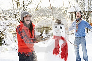 Young Couple Having Snowball Fight In Garden