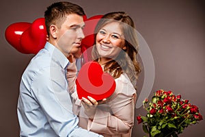 Young couple with heart shaped red balloons near grey wall