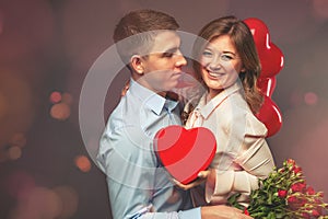 Young couple with heart shaped red balloons near grey wall