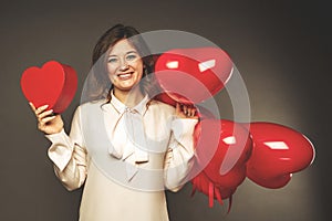 Young couple with heart shaped red balloons near grey wall