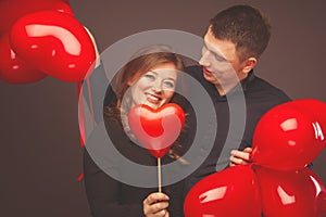 Young couple with heart shaped red balloons near grey wall