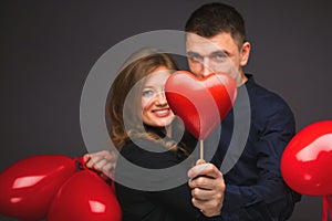 Young couple with heart shaped red balloons near grey wall