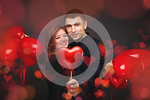 Young couple with heart shaped red balloons near grey wall