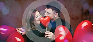 Young couple with heart shaped red balloons near grey wall