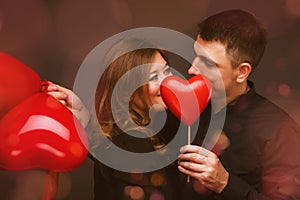 Young couple with heart shaped red balloons near grey wall