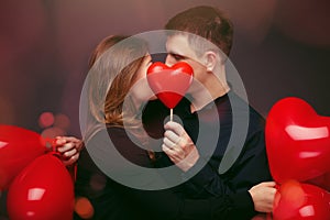 Young couple with heart shaped red balloons near grey wall