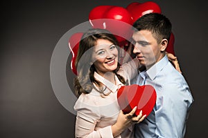 Young couple with heart shaped red balloons near grey wall