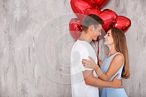 Young couple with heart shaped red balloons near grey wall