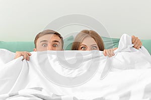 Young couple hiding together under blanket in bed at home