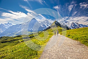 Young couple hiking in panorama trail leading to Kleine Scheidegg from Mannlichen with Eiger, Monch and Jungfrau mountain