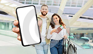 Young Couple Holding Blank Smartphone Screen at Modern Airport Terminal