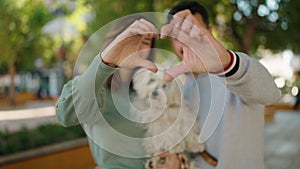 Young couple holding dog doing heart symbol with hands at park