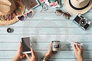 Young couple holding empty screen smart phone with travel summer accessories and items on wooden background