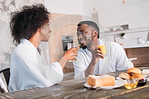 Young couple holding glasses with juice and sitting at table with toasts