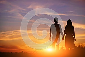 Young couple is holding hands on a background sunset silhouette