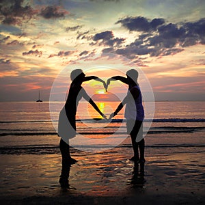 Young couple holding hands heart-shaped at sunset