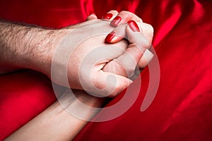 Young couple holding hands sensually on red silk bed