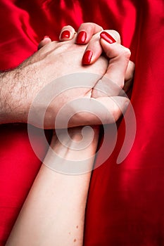 Young couple holding hands sensually on red silk bed
