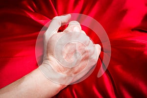 Young couple holding hands sensually on red silk bed