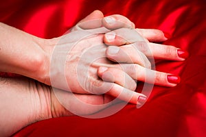 Young couple holding hands sensually on red silk bed