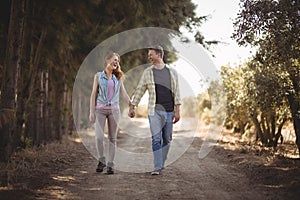 Young couple holding hands while walking on dirt road at olive farm