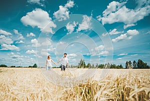 A young couple holding hands and walking through wheat field