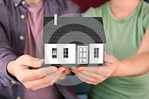 Young couple holding house model, closeup. Mortgage concept