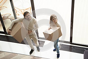 Young couple holding moving boxes entering new house, overhead v