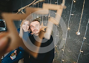 Young couple holding picture frame in the shape of Christmas tree against of christmas decorate on wall