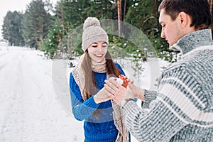 Young couple holding snow heart in winter forest. Hands in knitted mittens with heart of snow in winter day. Love