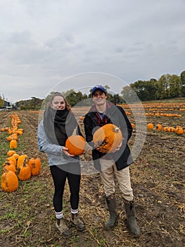 A young couple holds pumpkins at a pumpkin patch