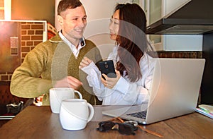 Young couple at home near the laptop are drinking coffee and laughing. Happy international couple make online purchase.