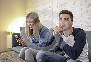 Young couple at home sofa couch with woman internet and mobile phone addiction ignoring her boyfriend feeling sad jealous frustrat