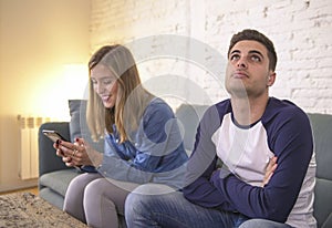 Young couple at home sofa couch with woman internet and mobile phone addiction ignoring her boyfriend feeling sad jealous frustrat