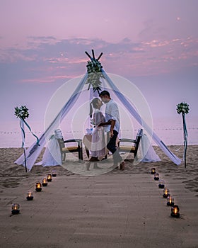 Young couple Honeymoon dinner by candle light during sunset on the beach, men and woman having dinner on the beach