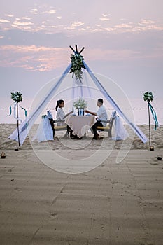 Young couple Honeymoon dinner by candle light during sunset on the beach, men and woman having dinner on the beach