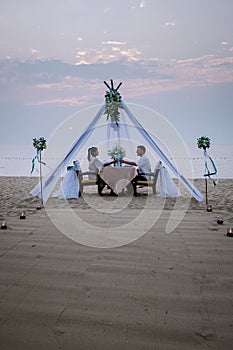 Young couple Honeymoon dinner by candle light during sunset on the beach, men and woman having dinner on the beach