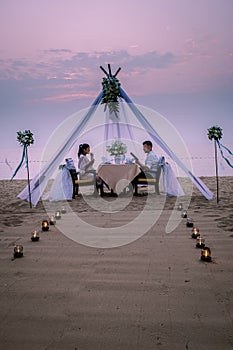 Young couple Honeymoon dinner by candle light during sunset on the beach, men and woman having dinner on the beach
