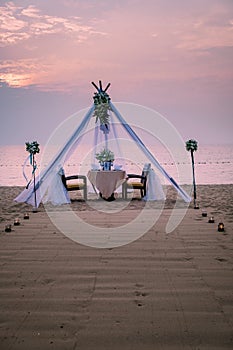 Young couple Honeymoon dinner by candle light during sunset on the beach, men and woman having dinner on the beach